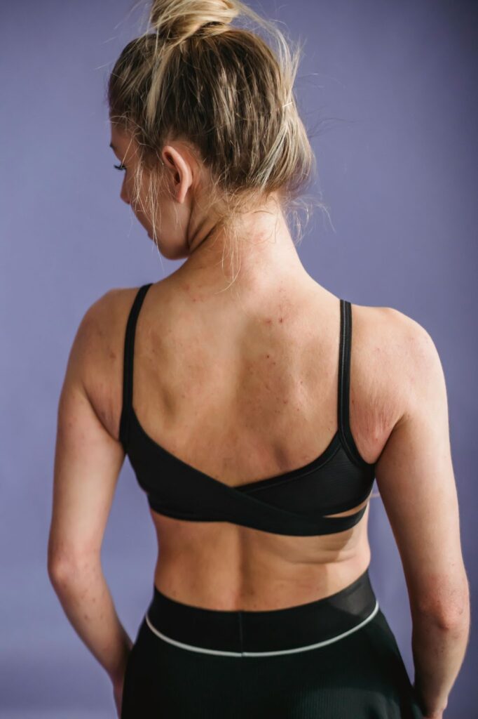 Woman in black sports bra with hair in a bun, showcasing activewear against a purple background.