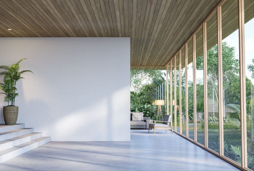 Modern living room with large windows, garden view, wooden ceiling, and minimalist decor featuring plants and seating.