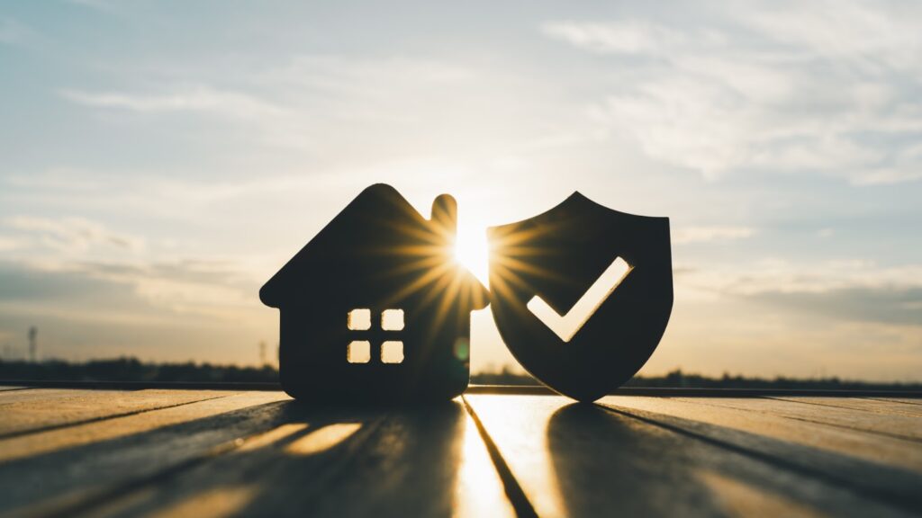 Silhouette of a house and shield with check mark against sunset, symbolizing home security and protection.