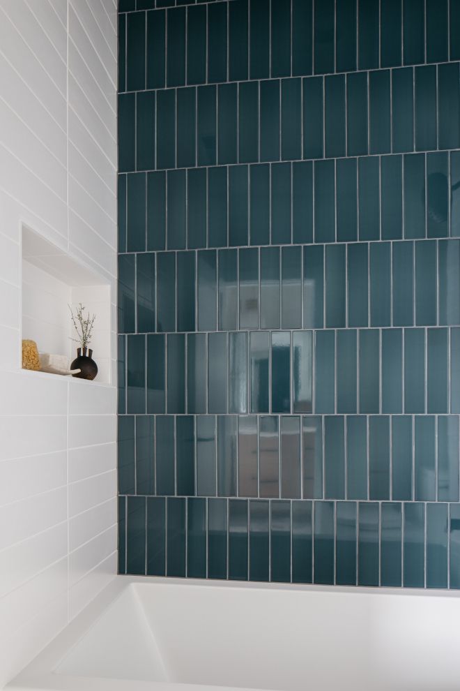 Modern bathroom with glossy teal subway tiles and white tub. Minimalistic design with built-in shelf décor.