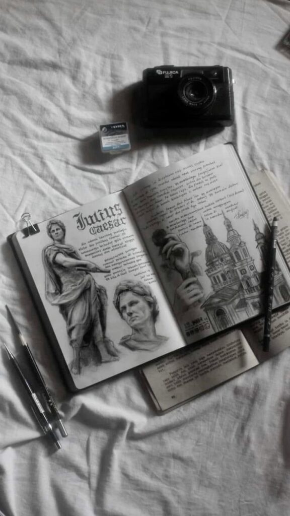 Artistic sketchbook with Julius Caesar illustrations, notebook, pens, vintage Fujica camera, and film on a white sheet.