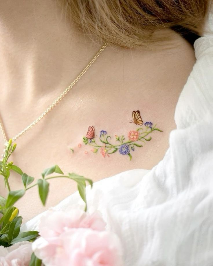 Delicate floral tattoo with butterflies on woman's collarbone, featuring colorful flowers and nature-themed design.