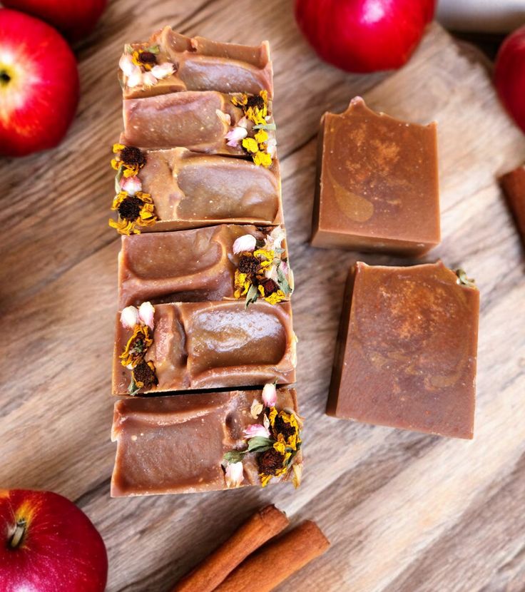 Handmade apple cinnamon soap bars with floral accents on a wooden table, surrounded by fresh apples and cinnamon sticks.