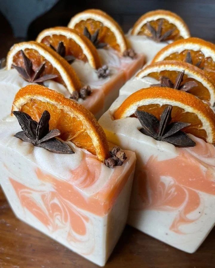 Handmade soap with dried orange slices and star anise, featuring a swirled white and orange design.