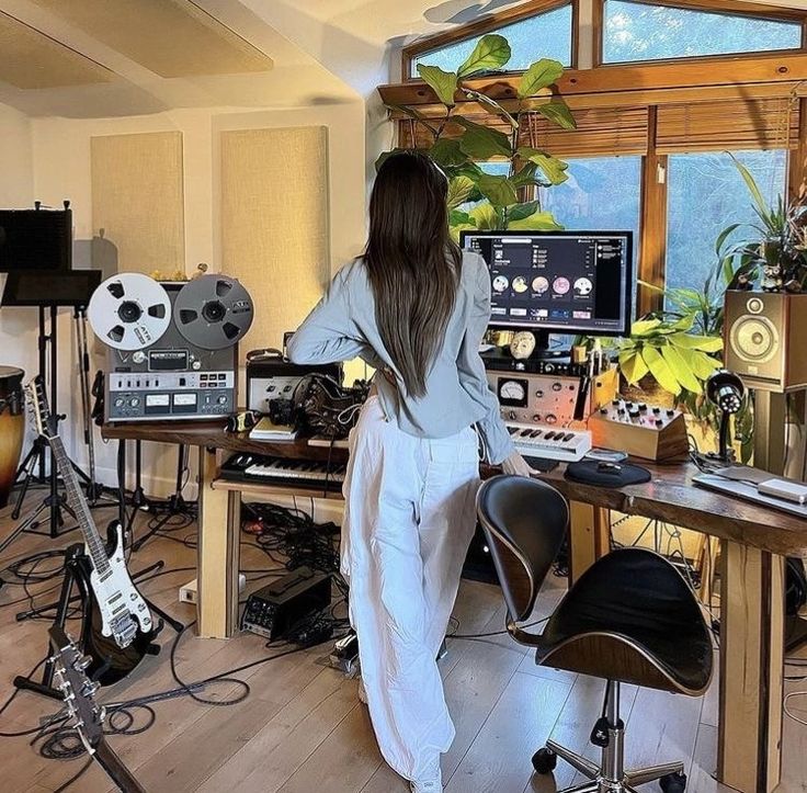 Woman in music studio with audio equipment, synthesizer, and computer monitors, working on sound production.