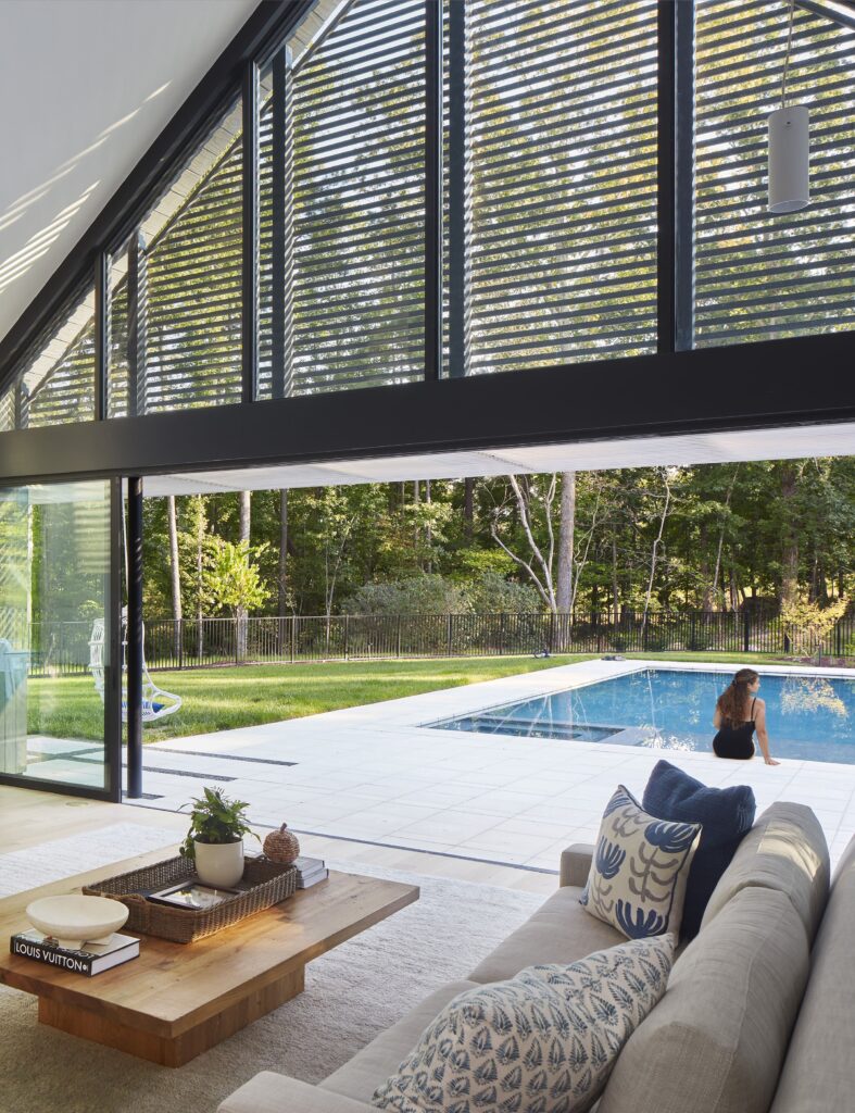 Modern living room with open view to pool and garden, featuring large windows, cozy sofa, and decorative cushions.