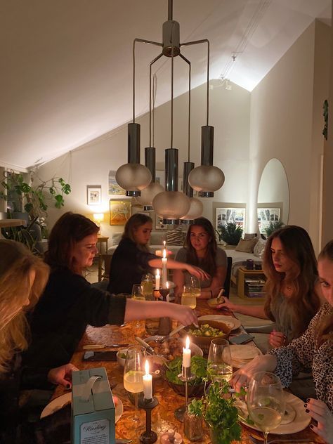 Group of friends enjoying a cozy dinner party with candles lit and warm lighting in a stylish dining room setting.