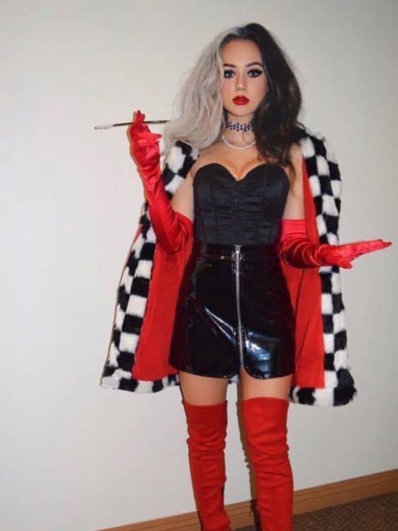 Person dressed in black and white coat, black corset, and red gloves, holding a cigarette holder, standing indoors.