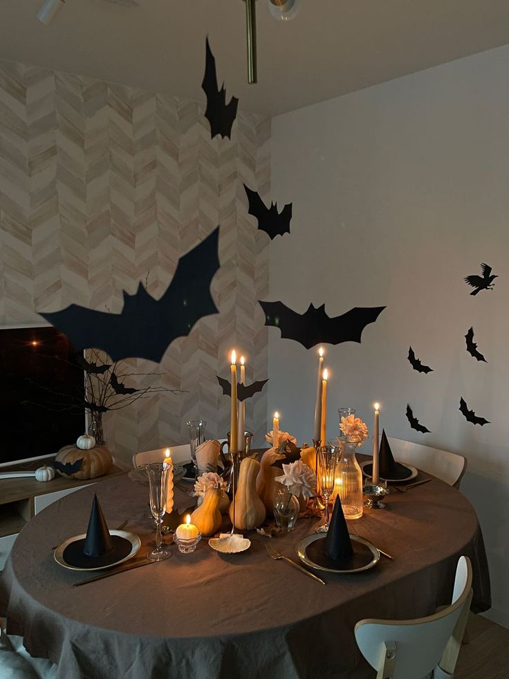 Halloween dinner table with candles, pumpkins, and bat wall decor for a spooky atmosphere.