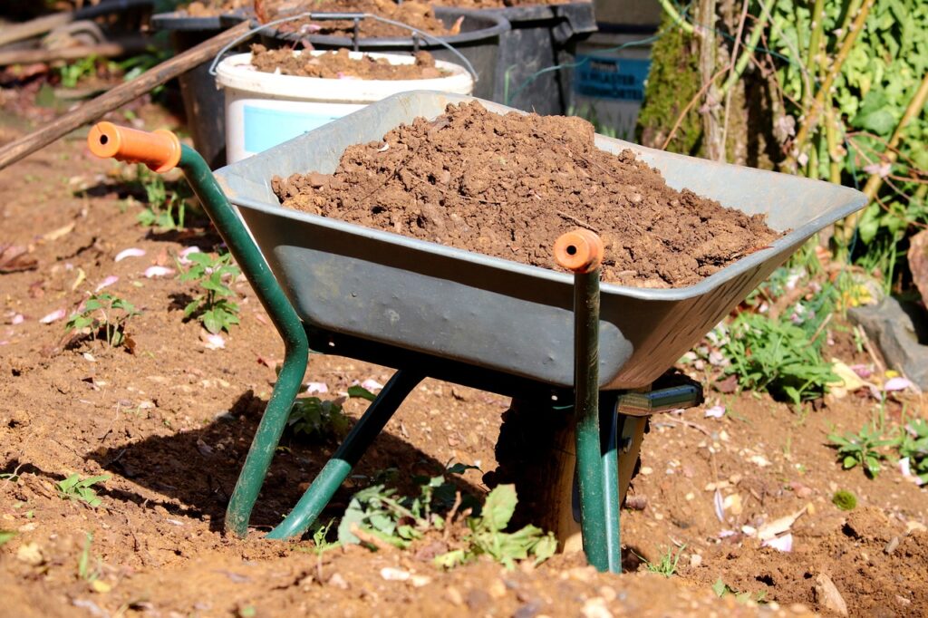 Wheelbarrow filled with soil in a garden, ready for planting tasks.