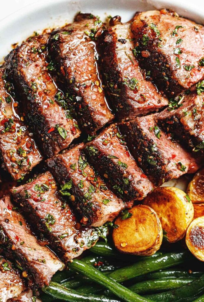 Juicy grilled steak slices with herbs, served with roasted potatoes and green beans on a white plate.