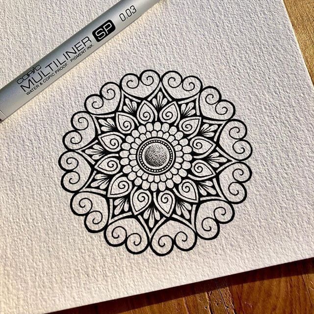 Intricate black and white mandala drawing on textured paper with fine liner pen.