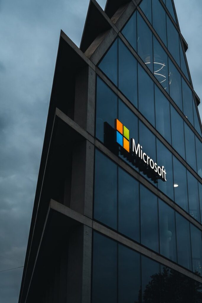 Glass building facade with Microsoft logo under cloudy sky, reflecting modern architecture and technology brand presence.