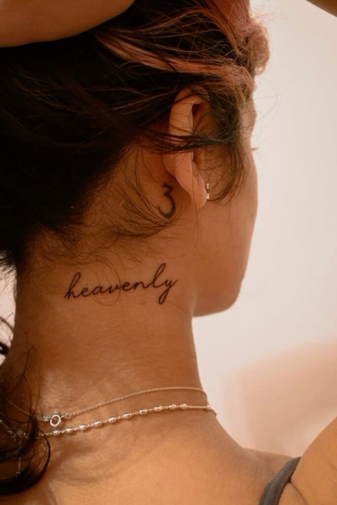 Woman with heavenly neck tattoo and number behind ear, wearing delicate necklaces.