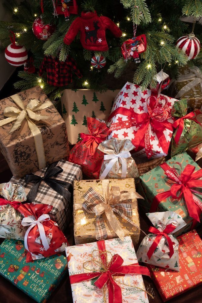 Christmas tree with festive ornaments and beautifully wrapped gifts in red, gold, and green under branches.