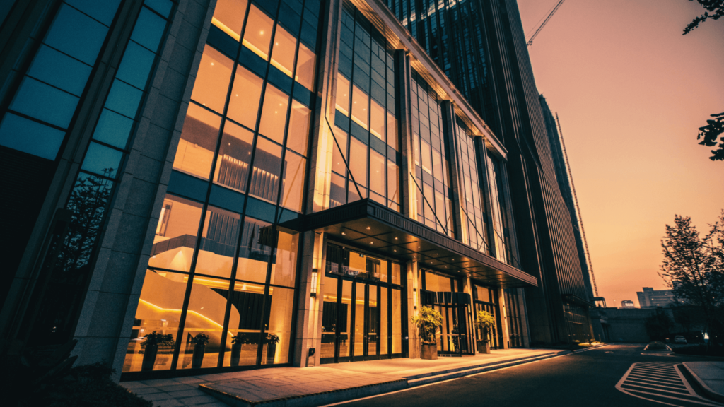 Modern office building exterior with glass facade, illuminated at sunset.