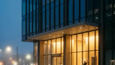 Night view of modern glass office building with illuminated lobby, wet street reflections and a worker cleaning the windows.