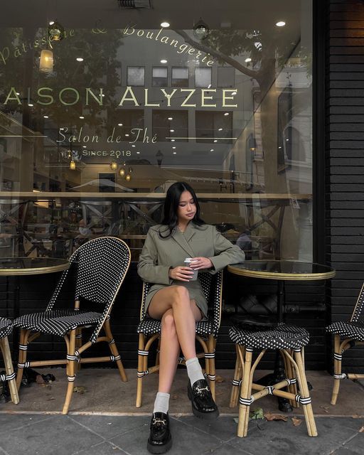 Woman enjoying coffee outside Parisian café Maison Alyzée, seated on a classic wicker chair, with stylish decor.