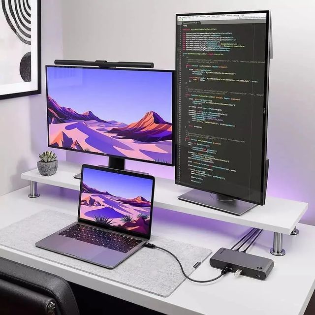 Dual-screen desk setup with laptop and monitor displaying coding and desert landscape wallpaper. Ideal for programmers.