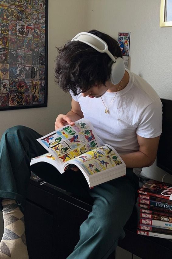 Person reading a comic book wearing headphones, surrounded by Marvel comic collections.