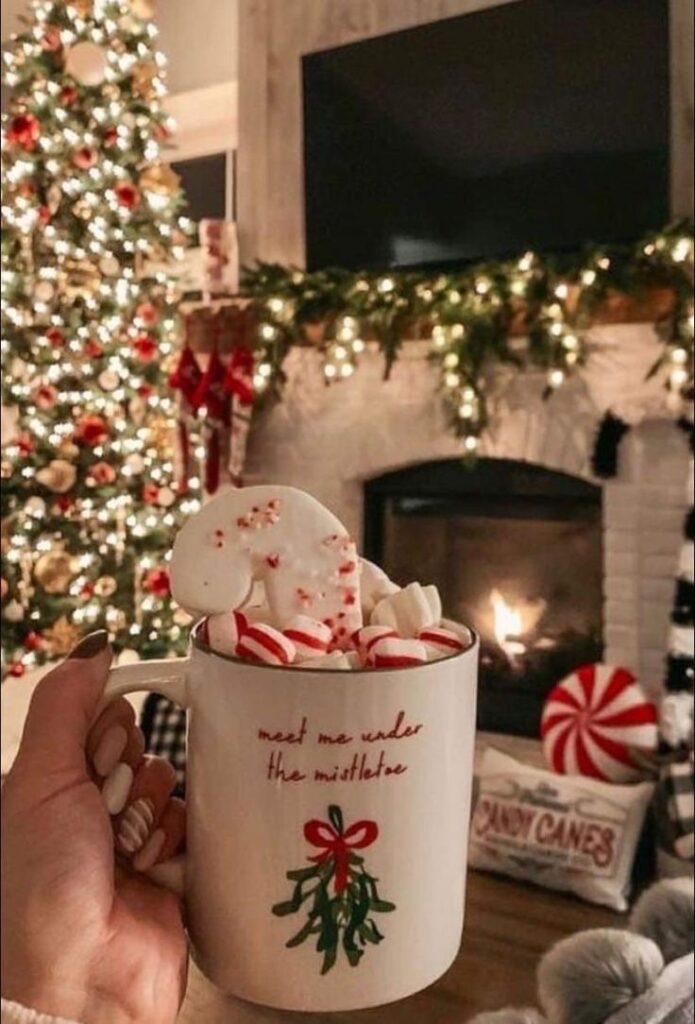 Cozy Christmas scene with hot cocoa and marshmallows by a fireplace and decorated tree.