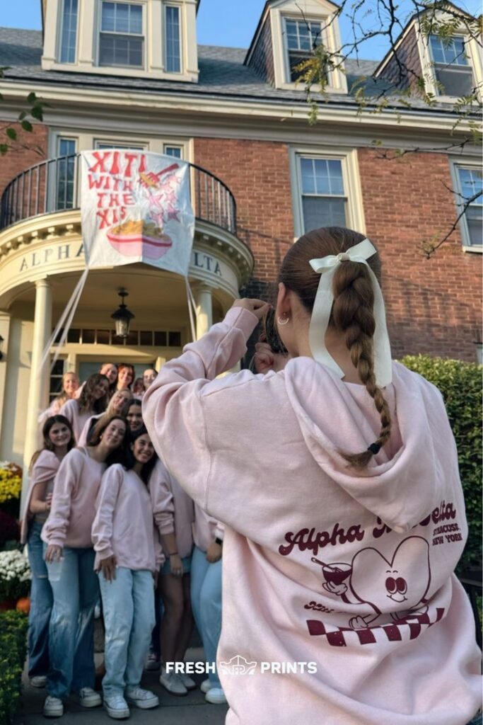 Group of people in matching pink hoodies at Alpha Xi Delta sorority house, capturing a fun moment during an event.