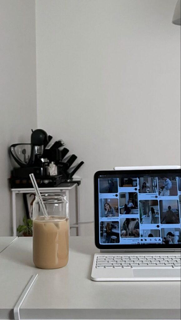 Tablet with images on screen and iced coffee in a glass jar on a desk in a minimalist home office.