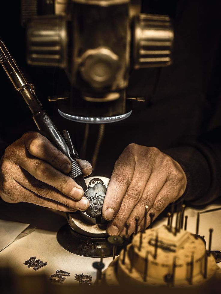 Craftsman engraving intricate details on a metal piece using precision tools under a magnifying lens.