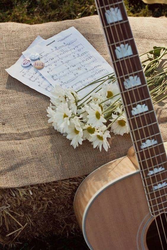 Acoustic guitar with sheet music and daisies on burlap, creating a rustic musical scene outdoors.