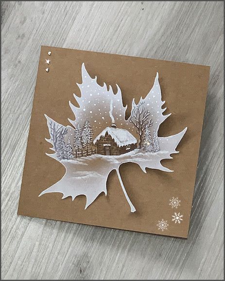 Leaf art with a winter scene painted on a maple leaf, featuring a cabin and snow-covered trees.