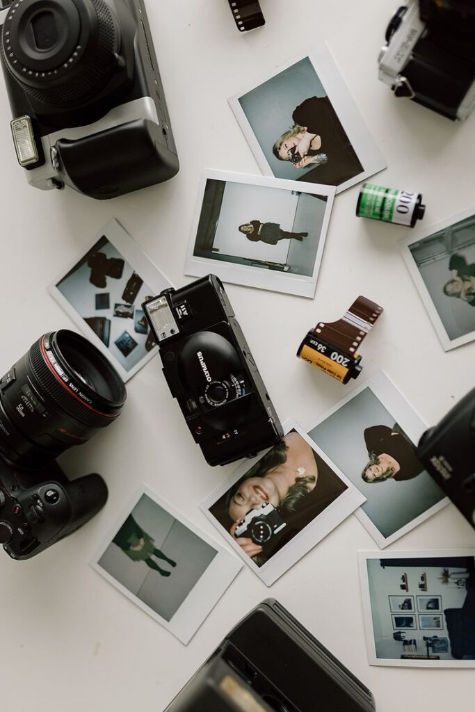 Vintage cameras with scattered Polaroid photos and film rolls on a white surface.