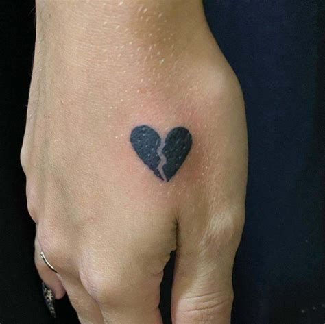 Broken heart tattoo on hand, symbolizing heartbreak or loss, black ink, small and detailed design.