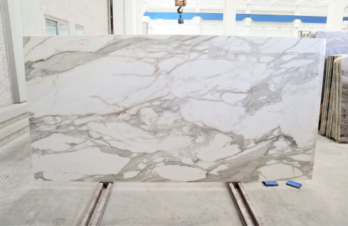 Large marble slab with white and grey veining displayed in a showroom. Perfect for countertops or flooring.