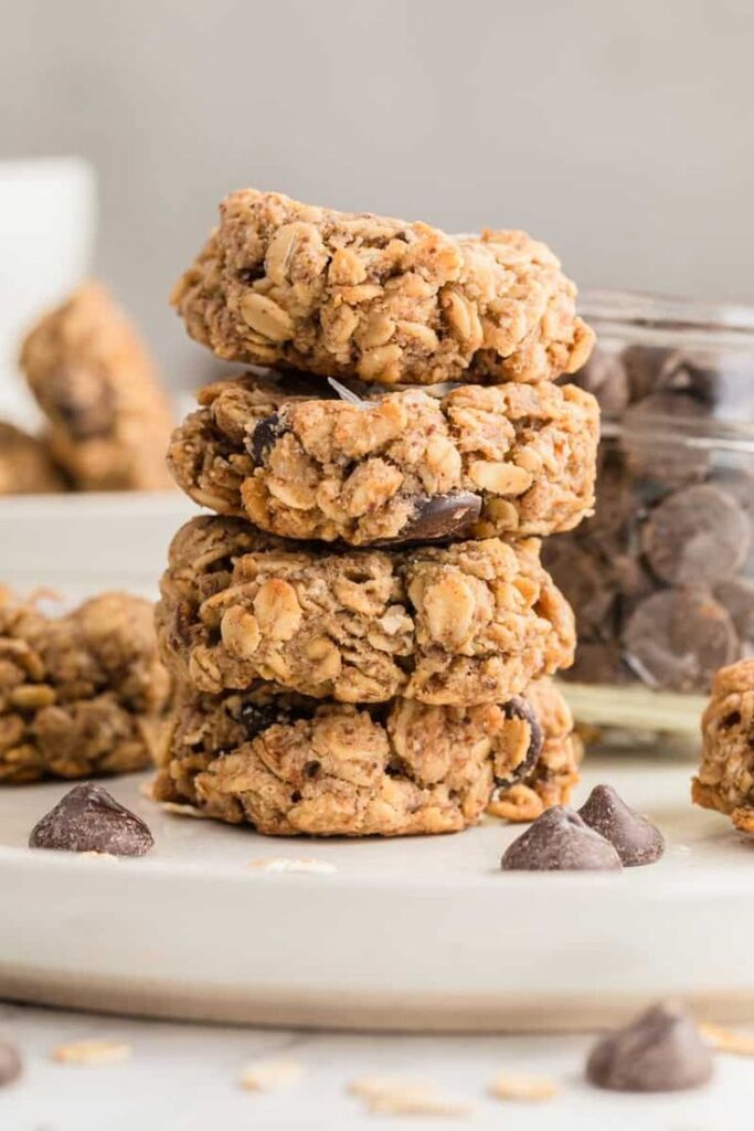 Stack of homemade oatmeal chocolate chip cookies on plate, with more chocolate chips in the background.