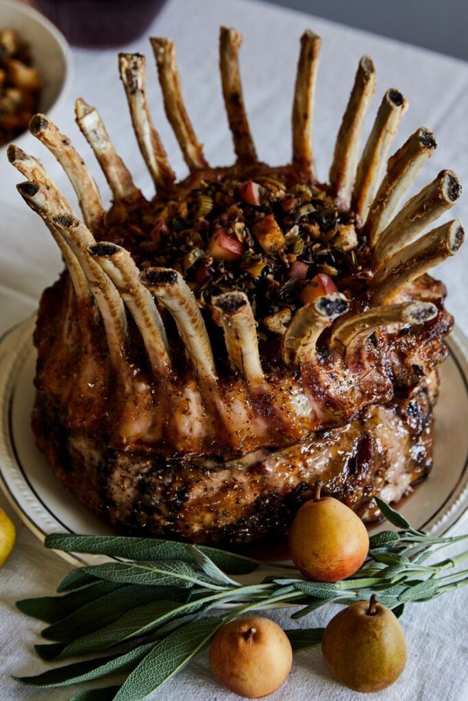 Succulent crown roast with sage and roasted vegetables, elegantly presented on a white tablecloth. Perfect holiday centerpiece.