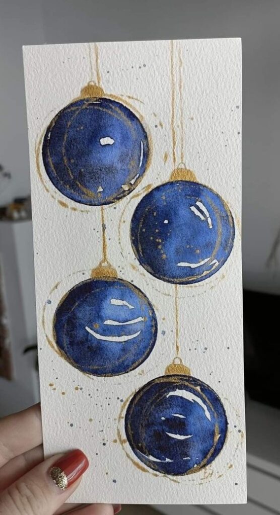 Watercolor painting of four hanging blue Christmas ornaments with gold accents on textured paper.