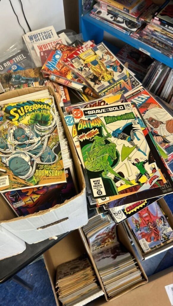 Collection of classic comic books including Superman and Batman displayed in boxes on a store shelf.