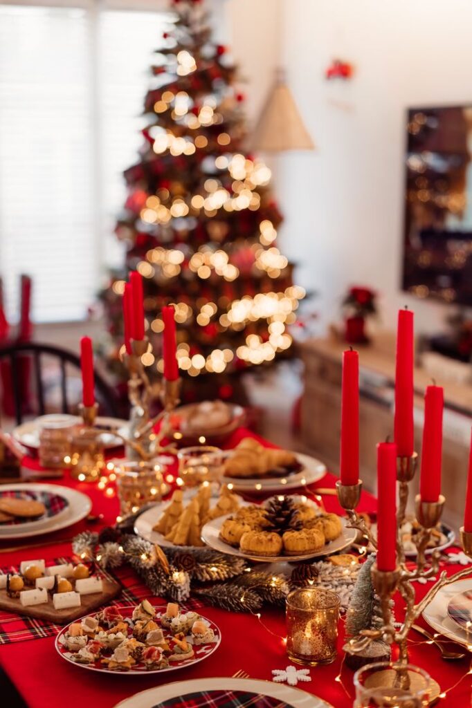 Festive Christmas table setting with red candles, delicious treats, and a lit Christmas tree in the background.