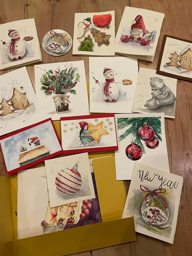 Assorted handmade Christmas cards with festive illustrations of snowmen, ornaments, and holiday themes on wooden floor.