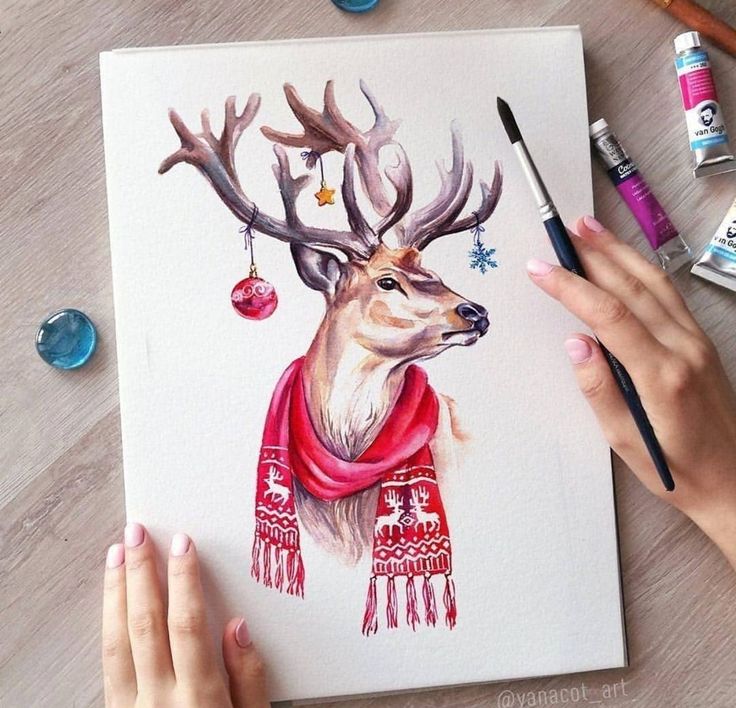 Watercolor painting of a reindeer wearing a red scarf with ornaments on antlers, artist's hands painting.