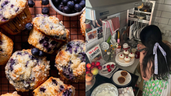 Blueberry muffins on a cooling rack next to a woman decorating cupcakes in a cozy kitchen setting.