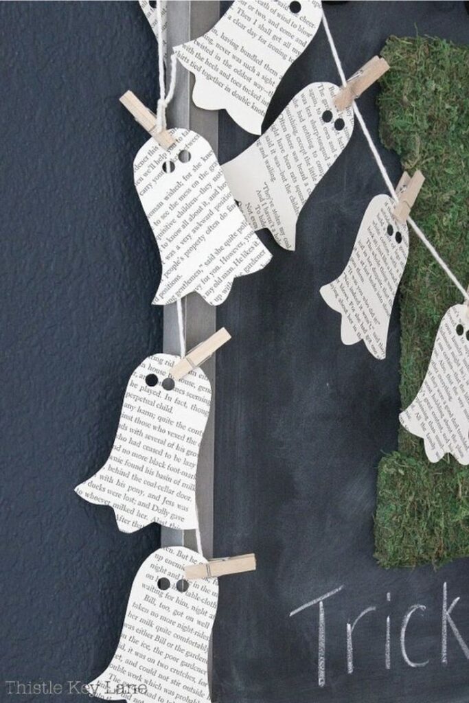 Halloween decor with ghost cutouts made from book pages, strung on a chalkboard with Trick written in chalk.