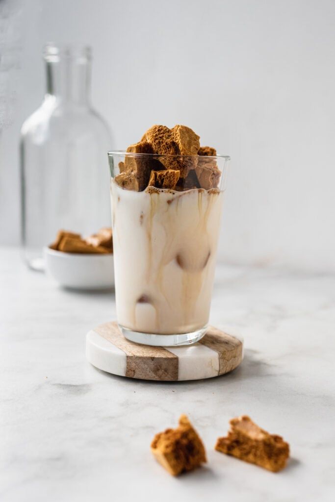 Iced coffee with milk and honeycomb chunks on marble coaster. Refreshing drink on a marble table.