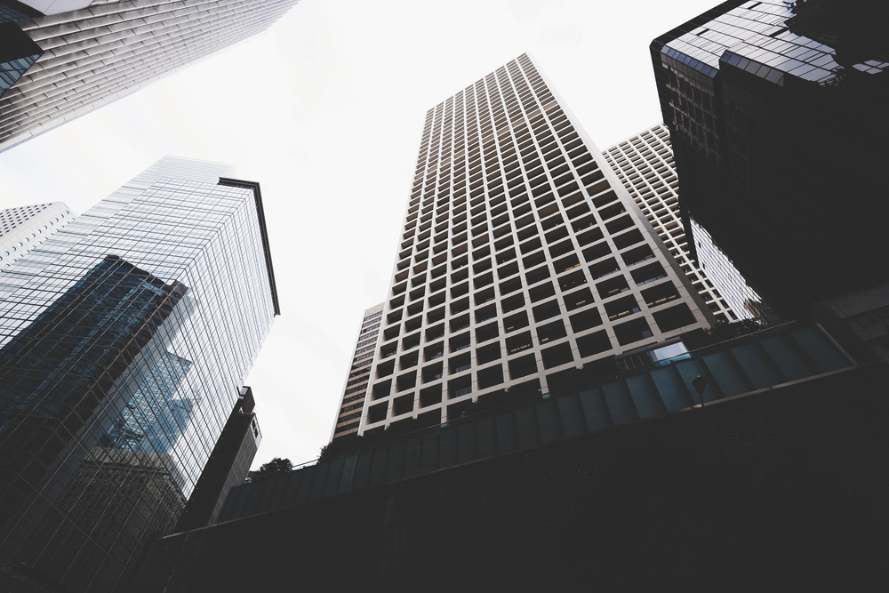 Sky-high city skyscrapers with grid windows against a bright sky, viewed from street level, showcasing urban architecture.