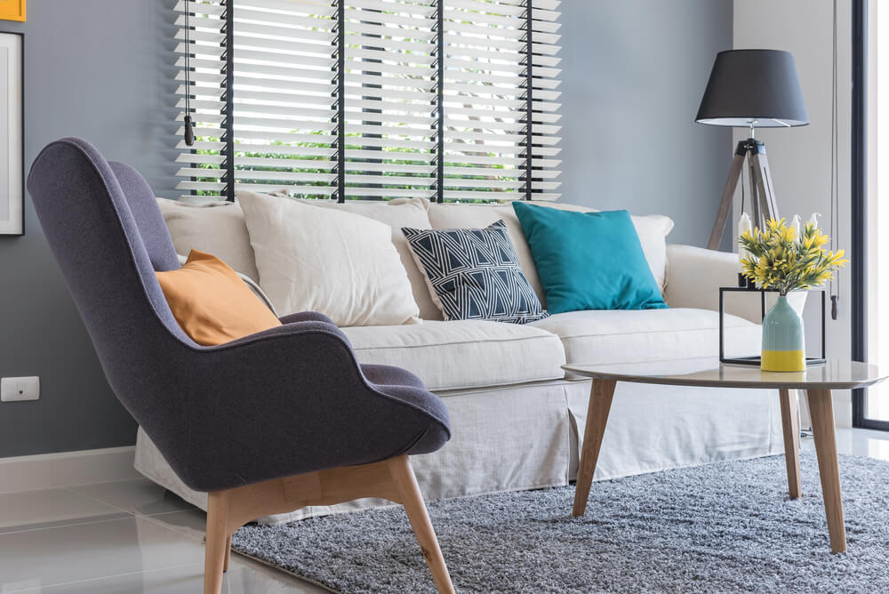 Modern living room with gray armchair, white sofa, colorful pillows, and stylish decor.