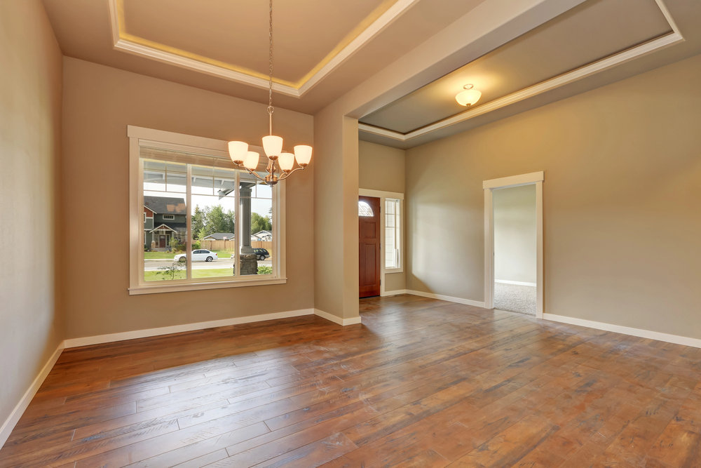 Spacious empty room with hardwood floors, large window, and elegant chandelier, perfect for a dining area or living space.