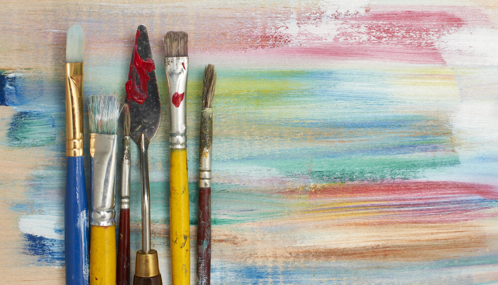 Artistic paintbrushes and palette knife on colorful painted surface background.