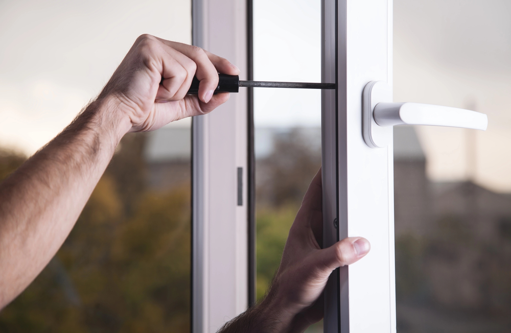 Person tightening screws on a white UPVC window frame with a screwdriver, ensuring security and maintenance.