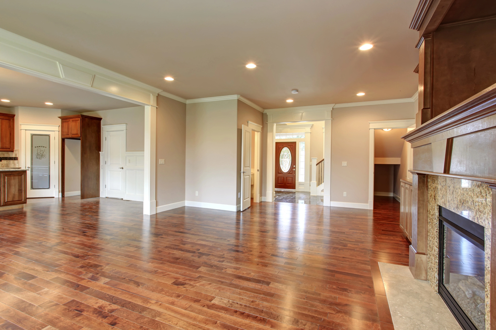 Spacious open living room with hardwood floors and a cozy fireplace, adjacent to a modern kitchen area.