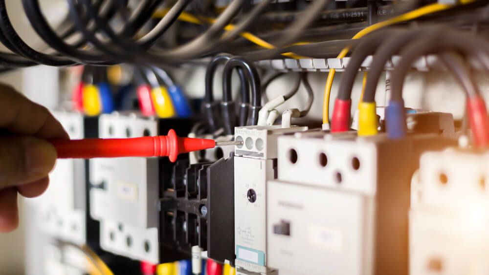 Electrician using tester on circuit board for maintenance and repair work.